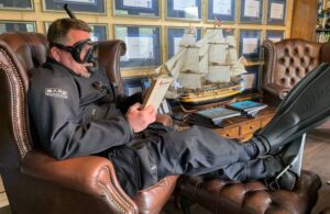 Diver sitting on couch reading book, lifestyle image