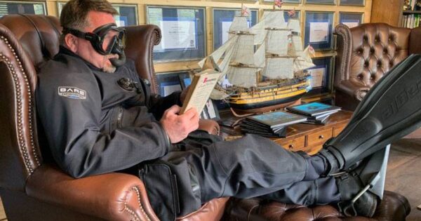 Diver sitting on couch reading book, lifestyle image